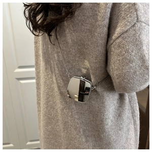 Détail d'un mini sac argenté effet miroir avec chaîne sur un pull en maille beige clair