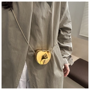 Détail d'un mini sac cœur doré métallique avec bandoulière en chaîne sur un trench-coat