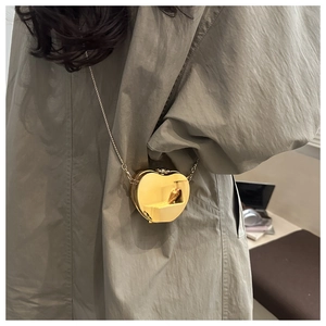 Glossy gold heart-shaped mini crossbody bag with a slim metal chain on a model