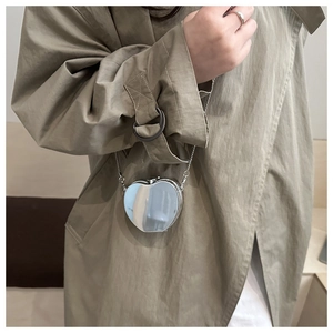 Silver apple-shaped mini crossbody bag with metal chain shown on a trench coat