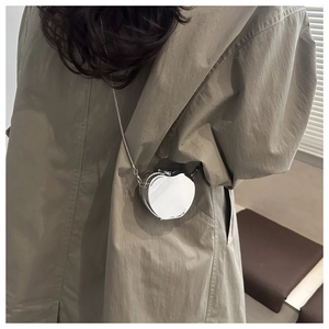 Detail of silver apple-shaped mirror mini bag with metal chain on trench coat