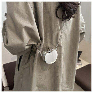 Mini sac bandoulière argenté en forme de cœur avec chaîne en métal porté sur un long manteau