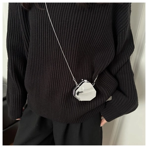 Close-up of a mini silver octagonal glossy metal bag with a sleek chain on a dark sweater