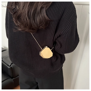 Detail of a geometric gold mini metal bag with a fine chain strap worn by a model