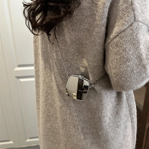 Sac bandoulière carré en acrylique argenté brillant avec chaîne porté sur un pull en maille