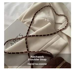 Detalle de bolso acolchado de ante marrón oscuro con cadena dorada sobre blazer blanco