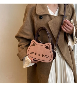 Détail du sac bandoulière rose en forme de chat avec des lanières marron sur un manteau