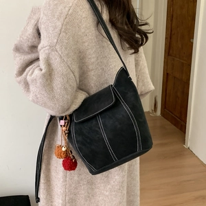 Schwarze matte Beuteltasche mit Kontrastnähten und Anhängern an der Schulter
