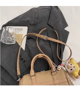 Detail of beige textured PU leather Boston bag with a bear charm on a grey blazer