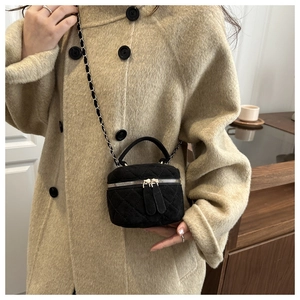 Detalle de un bolso tipo caja de ante negro acolchado con cadena sobre un abrigo beige
