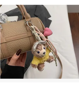 Detail of chic plush bear charm with pink heart on a beige textured handbag