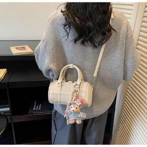 Detail of off-white lychee grain leather Boston bag with a plush bear charm on the side