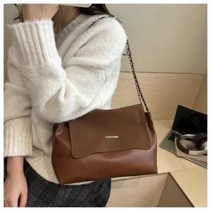 Close-up of brown shoulder bag with chain strap and printed fashion logo on flap