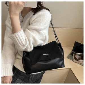 Detail of a black leather flap bag with white text print and chain strap over a sweater