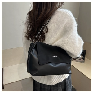 Detail of black matte leather tote bag with fashion text and woven chain strap on model