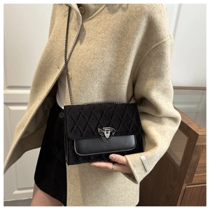 Detail of black quilted velvet crossbody bag with silver clasp worn on a beige coat