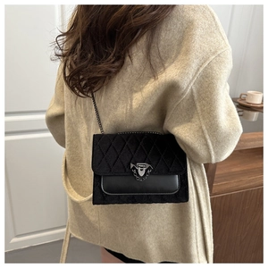 Close-up of black quilted velvet crossbody bag with chain strap on beige wool coat