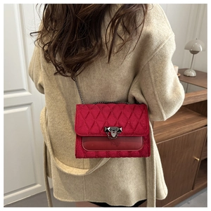 Detail of red quilted velvet crossbody bag with metal lock and chain on a beige coat