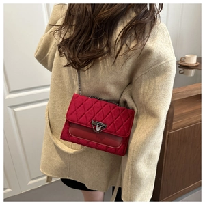 Detail of red quilted chain bag with silver lock worn over a beige wool coat