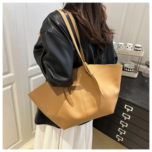 Détail d'un grand sac cabas en cuir camel avec texture grainée porté à l'épaule par un mannequin
