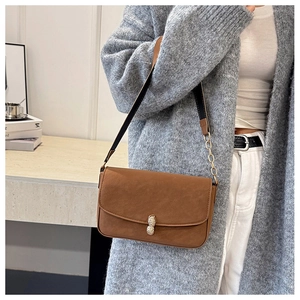 Detail of a brown suede crossbody bag with gold peanut-shaped buckle on a grey knitwear