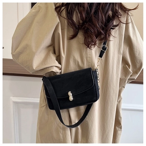 Detail of a black crossbody bag with a gold peanut-shaped lock and chain strap on a model