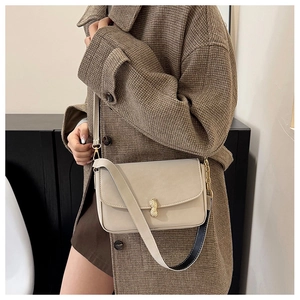 Detail of a beige shoulder bag featuring a unique gold peanut-shaped metal buckle and strap