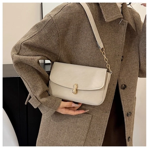 Detail of cream flap crossbody bag featuring a golden peanut metal clasp and chain strap