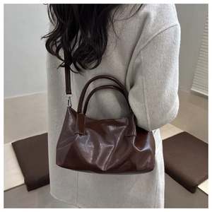 Detail of dark brown glossy tote bag showing textured patent leather and shoulder strap
