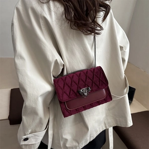 Elegant burgundy velvet quilted crossbody bag with metal lock shown on a beige coat