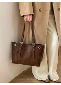 Detail of dark brown leather tote bag with metal rivets on a camel coat model