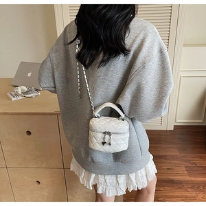 Detailed view of a white quilted vanity box bag with silver chain and heart charm