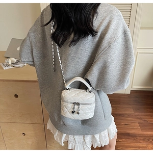 Detail of white quilted mini box bag with silver chain strap worn by a model