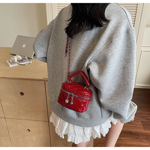 Close-up of red quilted patent leather mini box bag with heart zipper and chain strap