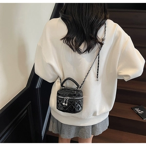 Detail of a black quilted mini box bag with silver chain strap shown on a model