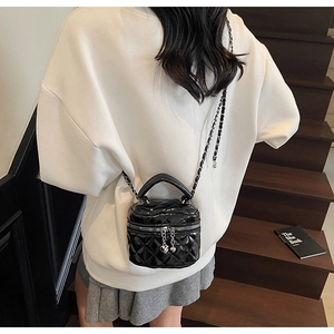 Detail of mini black quilted patent leather bucket bag with gold heart charm and chain