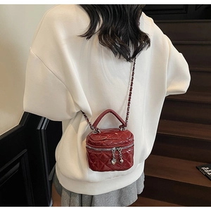 Quilted wine red crossbody bag with heart pendant and chain strap worn by a model