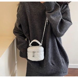 Detail of white quilted mini box bag with gold chain strap and heart charm