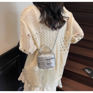 Close-up of a mini silver quilted box bag with chain strap worn over a white knit top