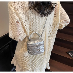 Close-up of silver quilted box bag with heart pendant and metal chain strap detail