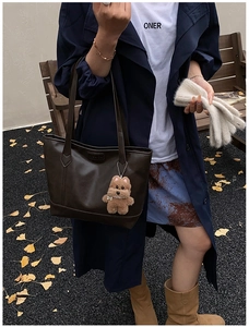 Detail of dark brown tote bag with plush charm on navy coat and printed skirt background