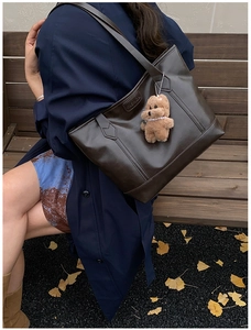 Detail of dark brown tote bag on model showing large capacity and bear charm