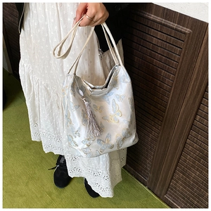Detail of elegant white handbag featuring blue butterfly embroidery and long side tassels