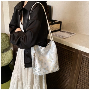 Close-up of white silk tote bag featuring exquisite blue and gold butterfly embroidery