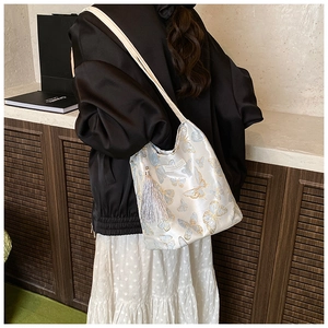 Détail du sac seau en satin brodé avec motifs papillons bleus et pompon en soie élégant