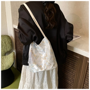 Détail de la broderie papillon sur le sac seau en satin ivoire avec pompon