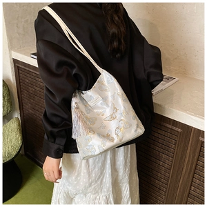 Détail du sac seau crème avec broderie papillon élégante et long pendentif à pompon