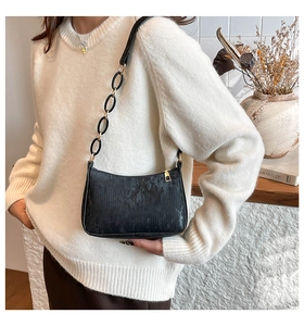 Close-up of black textured underarm bag with gold chain strap on a knit sweater