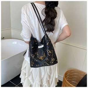 Detail of black bucket bag featuring gold butterfly print and fashion label