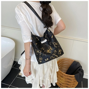 Détail d'un sac cabas noir avec motifs de papillons dorés et pompons en soie grise